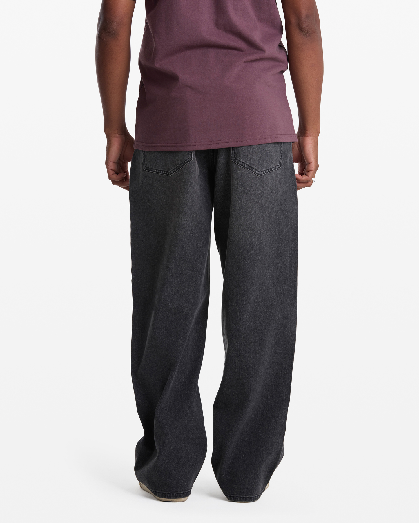 A person stands facing away from the camera, wearing Volcom's Men's Chillow Denim jeans with a maroon shirt, against a plain white background.