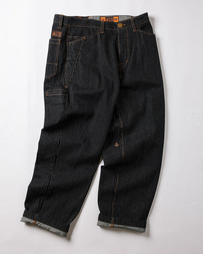 The Volcom Men's Dialed Work Pants feature black denim with white pinstripes, orange stitching, rolled cuffs, multiple pockets, and a metal waist button—combining durability and style for perfect workwear.