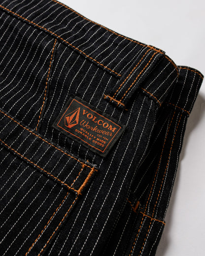 Close-up of Volcom Men's Dialed Work Pants in black pinstripe canvas with orange stitching and a brown Volcom Workwear label above the pocket, folded neatly on a white surface.