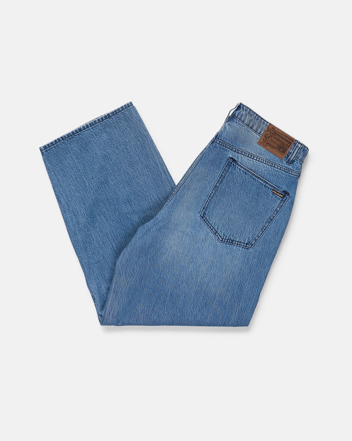 A pair of Volcom Men's Chillow Denim Vs in blue, folded neatly with a visible back pocket and brown leather patch on the waistband, displayed on a white background.