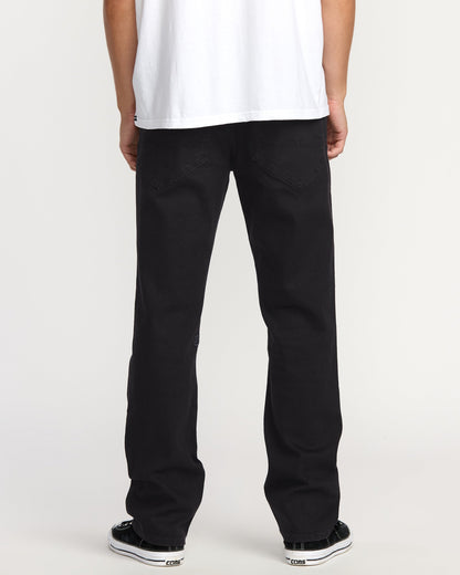 A person faces away, wearing a white T-shirt, black-and-white sneakers, and Volcom Men's Volcom Entertainment Pennywise Denim Pants, against a plain light backdrop.