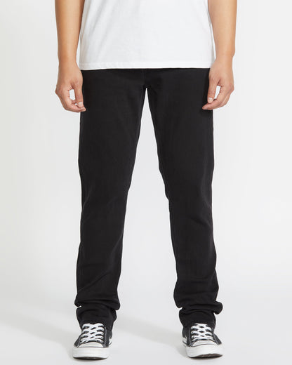 A person stands facing forward, wearing a white T-shirt, Volcom Vorta Denim black jeans, and black-and-white sneakers against a plain white background. The image is cropped from the shoulders down.