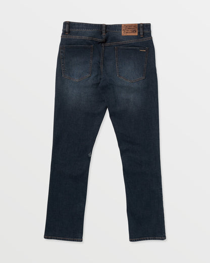 The Volcom Men's Vorta Denim jeans in dark blue are shown laid flat from the back on a white background. They feature two back pockets, brown stitching, a brown leather waistband patch, and straight-cut legs.