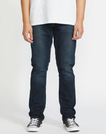 Wearing Volcom's Men's Vorta Denim jeans, a person stands against a plain white background. The image is cropped from the shoulders down and also shows a white t-shirt and black-and-white sneakers.