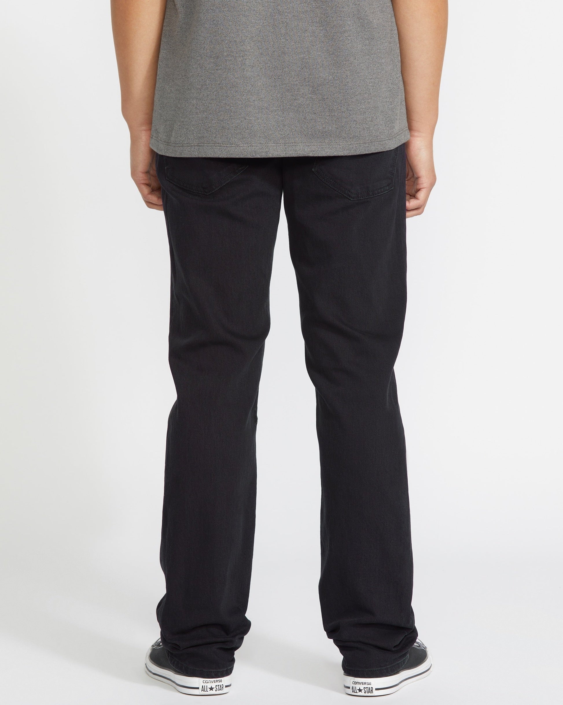 A person faces away from the camera, wearing a gray t-shirt, Volcom Men's Solver Denim Pant in black, and black-and-white sneakers, posed against a plain white background.