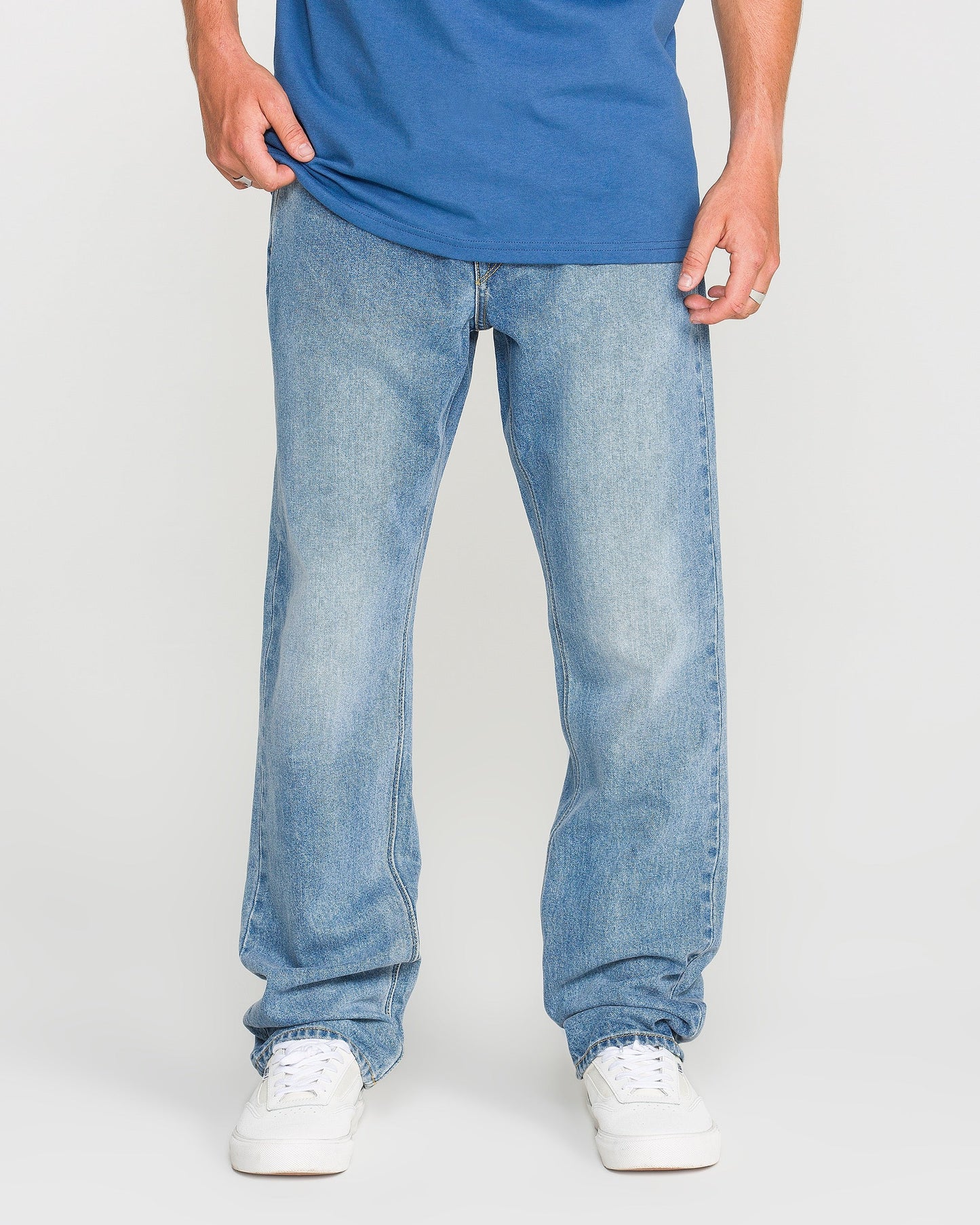 A person wearing a Freedom Blue T-shirt, Volcom Men's Solver Denim Pants in light blue stretch denim with a modern straight leg cut, and white sneakers stands facing forward against a plain white background. Their head is not visible in the image.