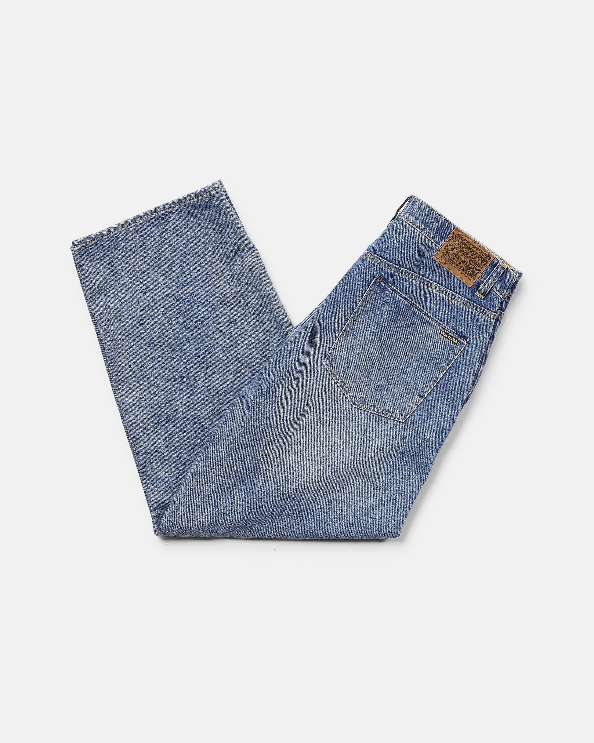 A pair of Volcom Men's Chillow Denim Pants in Euro Light Blue, low-rise and neatly folded with a brown leather patch on the waistband and a visible back pocket, set against a plain white background.