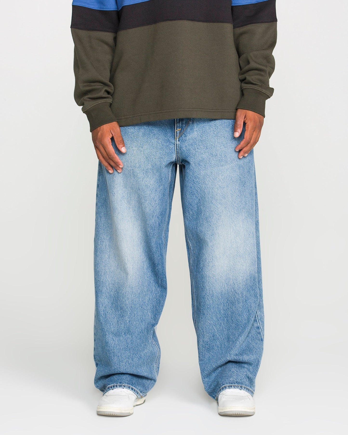Model showcases the Volcom Men's Chillow Denim Pants in Euro Light Blue—a baggy, low-rise fit—paired with a long-sleeve shirt and white shoes. Only the body from shoulders down is visible, photographed against a plain white background.
