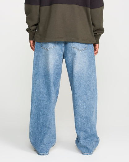 A person stands with their back to the camera against a plain white background, wearing a dark olive green sweatshirt and Volcom Men's Chillow Denim Pants in a loose-fitting, Euro Light Blue wash.