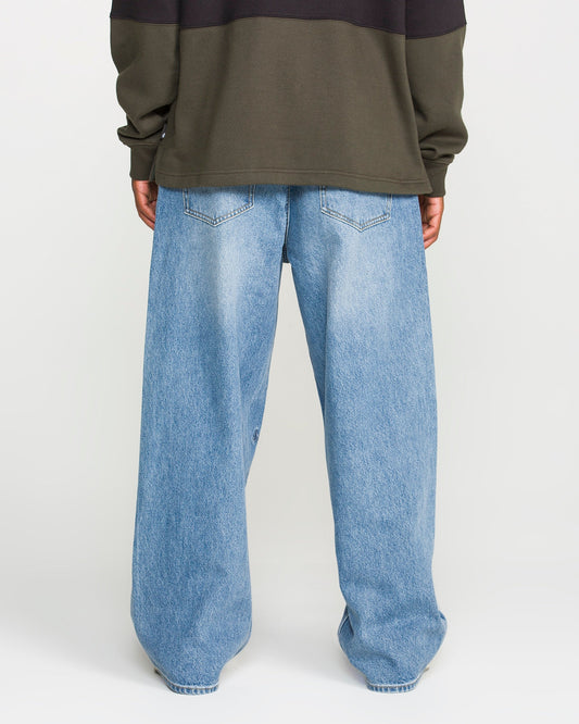 A person stands with their back to the camera against a plain white background, wearing a dark olive green sweatshirt and Volcom Men's Chillow Denim Pants in a loose-fitting, Euro Light Blue wash.