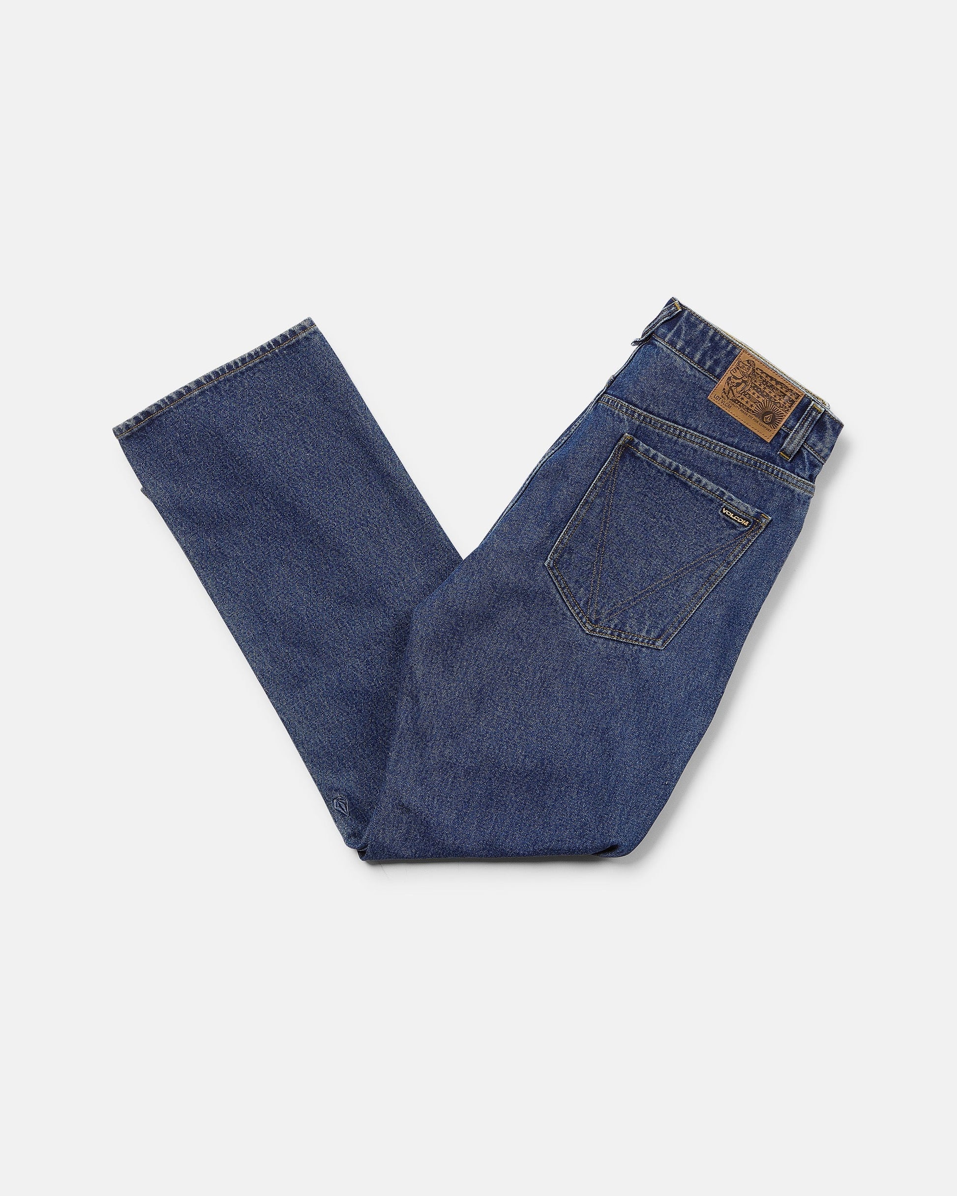 Men's Pipe Dreams Denim Pants by Volcom, crafted from dark indigo denim in a relaxed straight fit, are folded neatly to display the back pocket and brown leather Volcom brand patch on the waistband, set against a plain white background.