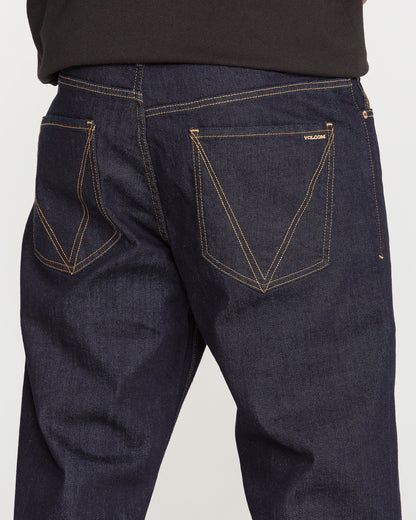 Close-up of the back of a person wearing Volcom Men's Pipe Dreams Denim Pants in dark blue indigo stretch denim, featuring contrasting orange stitching and two back pockets—one adorned with a small “Volcom” label that showcases the brand's signature details.