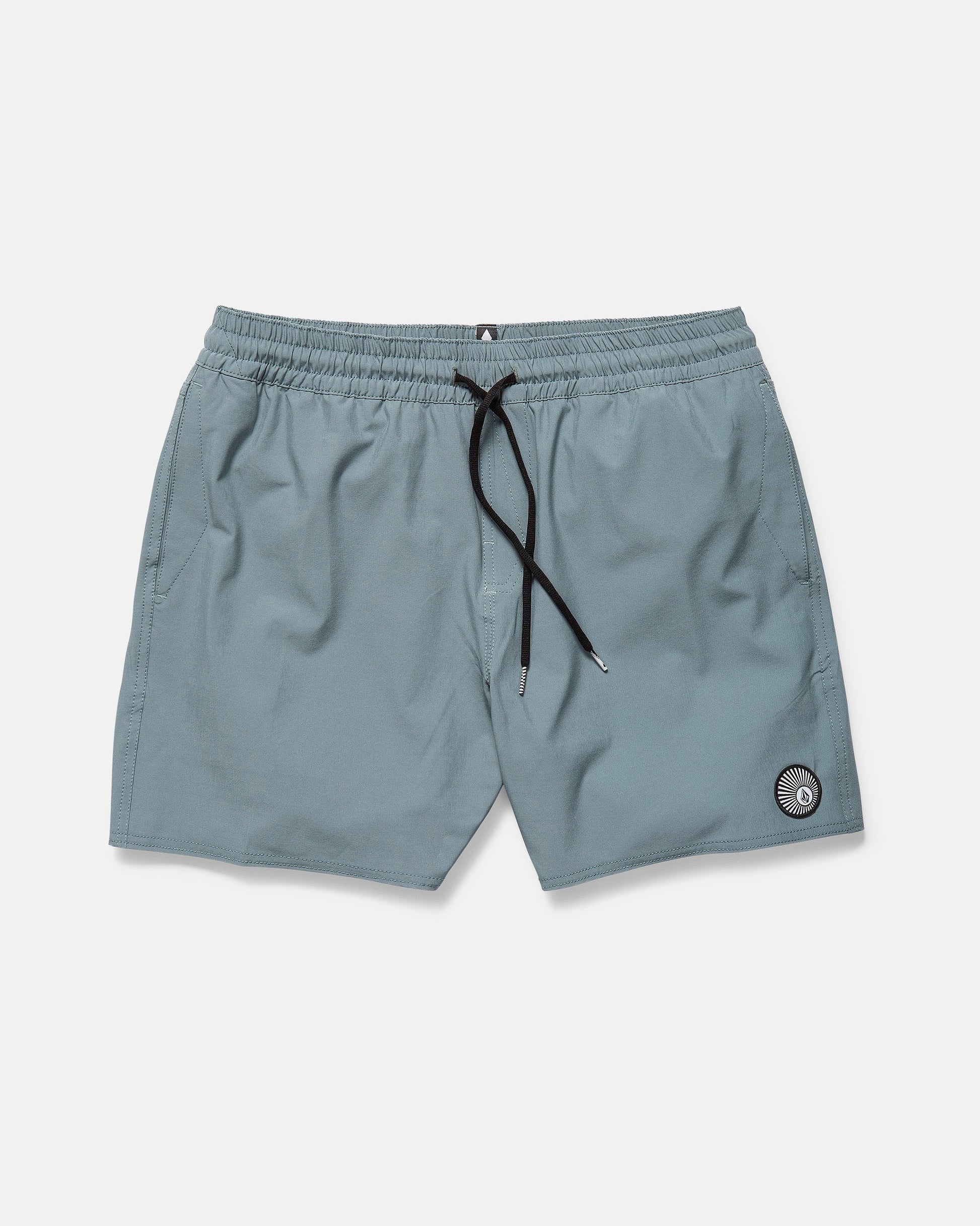 The Volcom Men's Lido Solid 16" Trunk in light blue features an elastic waistband, black drawstring, side pockets, and a small circular patch near the left hem. The shorts are displayed flat on a plain white background.