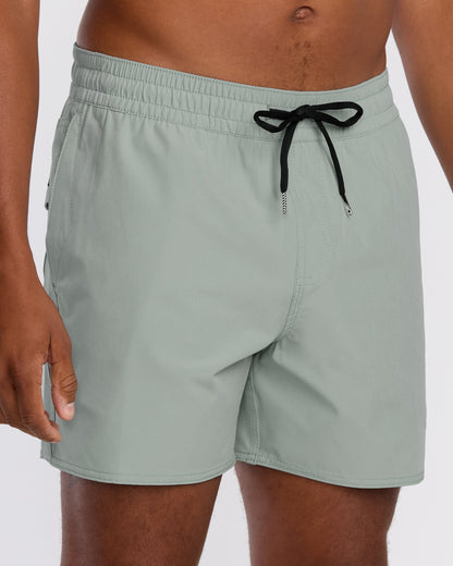 A person wears Volcom Men's Lido Solid 16" Trunks in light green, made from recycled polyester with 2-way stretch. The image shows only the lower torso and upper legs, set against a plain white background.