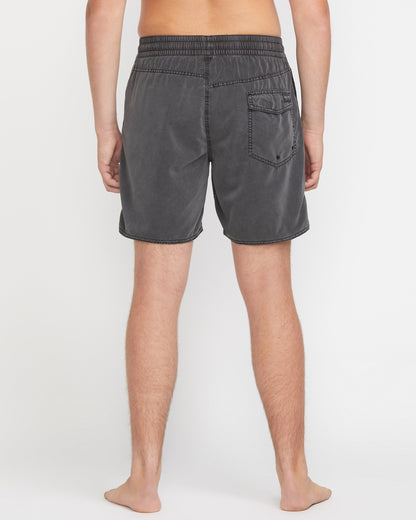 A person stands barefoot facing away, wearing Volcom Men's Center Elastic Waist 17" Trunk in charcoal gray with a single back pocket and mechanical stretch; the background is plain white.