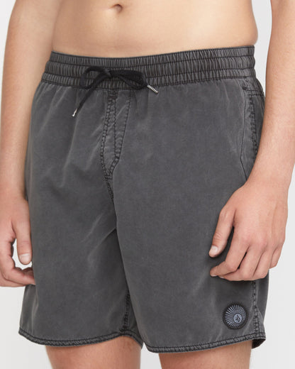 A person is shown from waist to mid-thigh wearing Volcom Men's Center Elastic Waist 17" Trunk swim shorts in dark gray, featuring an elastic waistband, mechanical stretch, and a small circular patch on the left leg.