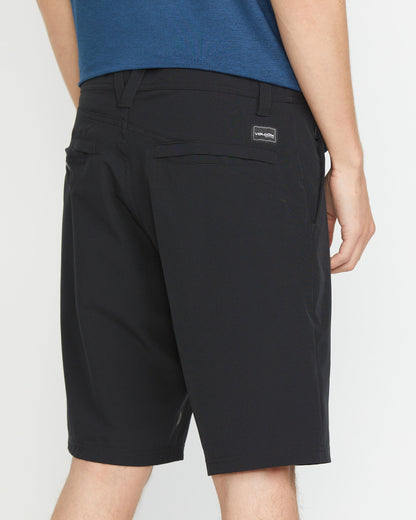 A person in a blue shirt and black Volcom Men's Frickin Cross Shred 20" Shorts is shown from the back, featuring a visible Volcom logo patch above the right back pocket.