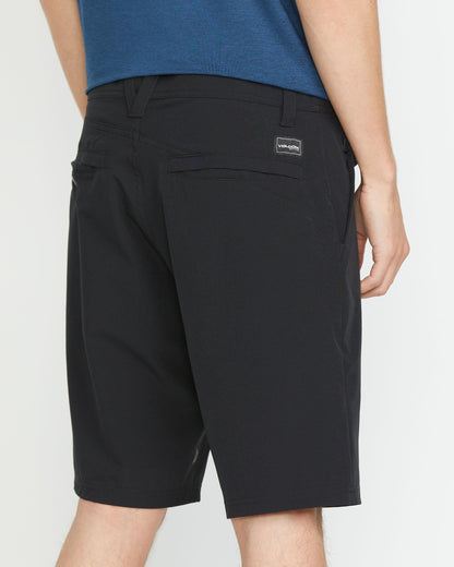 A man wearing a blue shirt and black Volcom Men's Frickin Cross Shred 20" Shorts stands facing away, displaying the shorts' two rear pockets and a small rectangular brand label above the right pocket.