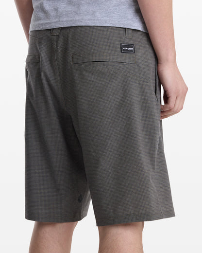 A person shown from the waist down and back wears gray plaid Volcom Men's Mix Frickin Cross Shred Shorts and a gray shirt, with their right hand resting by their side.
