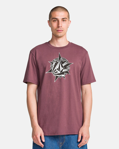 A man stands against a white background wearing the Volcom Men's Yoink Short Sleeve Tee, a classic fit maroon crew neck with a bold black and white geometric compass and diamond logo on the chest. Made from 100% cotton for comfort.