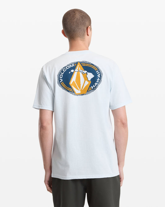 A person viewed from behind wears the Volcom Men's Loopy Short Sleeve Tee in light blue, featuring a circular graphic with "VOLCOM HAWAII" and a stylized yellow and white design on the back.