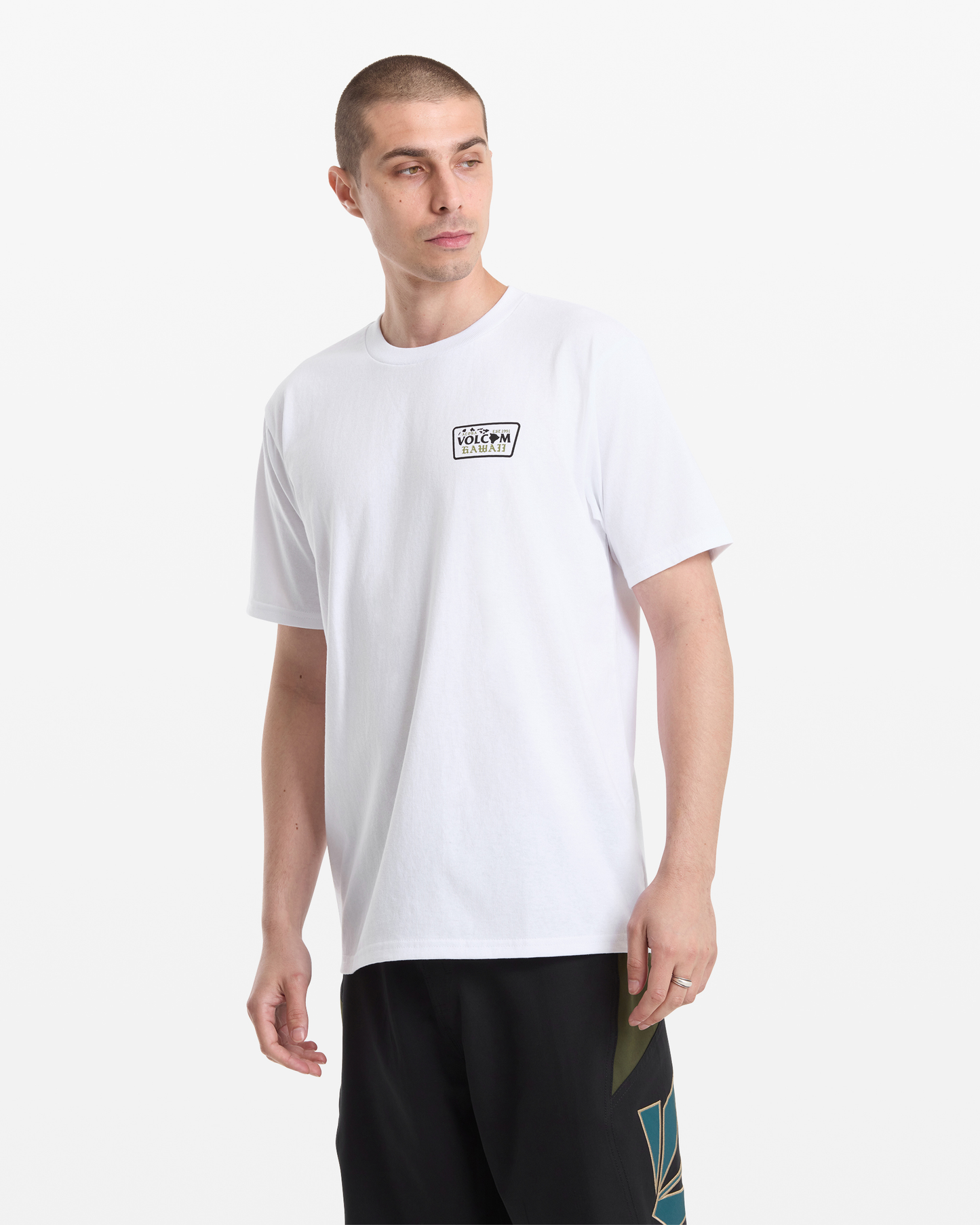 A man with short hair wears the Volcom Men's Dispatch Short Sleeve Tee, featuring a small rectangular chest logo, and black shorts. He stands against a plain white background, looking slightly to his left.