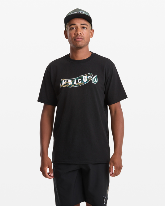 A man wearing a black Volcom Men's Featured Artist Parillo Short Sleeve Tee, black shorts, and a black Volcom cap stands facing forward against a plain white background.