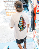 Wearing the Volcom Men's Star Shields Featured Artist Exp Short Sleeve Tee and a cap, a person walks down colorful steps into the sunlit outdoors. The tee’s bold star shields and graphic art add artistic flair to the scene.