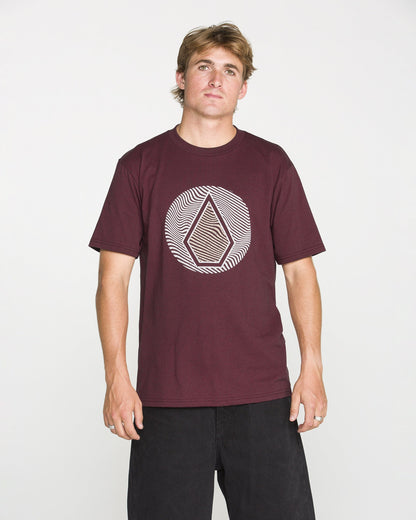 A man is wearing the Volcom Men's Wave Stone Short Sleeve Tee in burgundy, crafted from premium ring spun cotton and featuring the signature geometric Wave Stone design on the chest. He stands against a plain white background, facing the camera with a neutral expression.