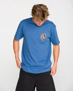 A person wearing the Volcom Men's Ringafire Short Sleeve Tee, crafted from premium ring spun cotton and adorned with a vibrant circular chest logo, looks down while standing against a plain white background.