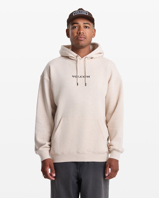 A person wearing a light beige Men's Volcom Stone Pullover by Volcom, dark pants, and a brown cap stands facing forward against a plain white background.