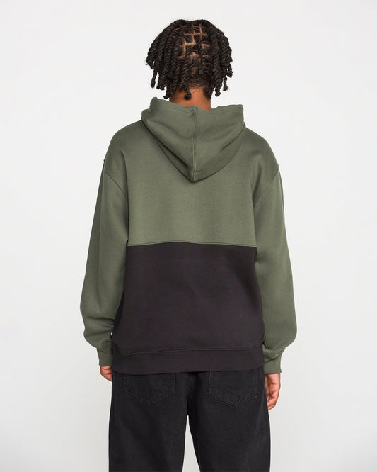 A person with braided hair is seen from behind against a plain white background, wearing the Volcom Men's Long Division Pullover. The hoodie showcases green and black colorblocked panels and is paired with black pants. Crafted with REPREVE recycled fibers, this eco-conscious pullover combines style and sustainability.