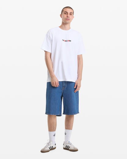 A person stands against a white background wearing a Men's Featured Artist Seth Conboy Loose Short Sleeve Tee by Volcom, knee-length blue denim shorts, white socks with a logo, and gray Adidas sneakers.
