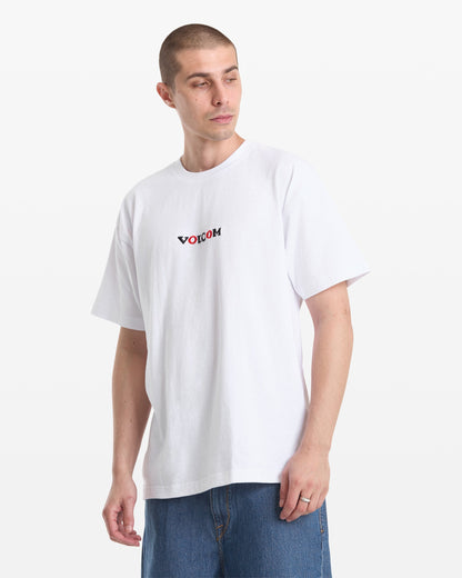 A man in a Volcom Men's Featured Artist Seth Conboy Loose Short Sleeve Tee and blue jeans stands against a plain white background, looking to the side with a neutral expression.