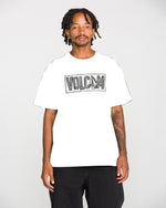 A man with short dreadlocks and a mustache wears the Volcom Men's Studded Short Sleeve Tee, crafted from heavyweight premium cotton and featuring a soft-hand screen print. He pairs it with black pants and stands against a plain light background.