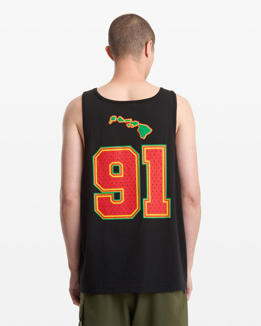 A person wearing the Volcom Men's Swish Tank, featuring a large red and yellow 91 and Hawaiian Islands graphic on the back, stands against a plain white background.