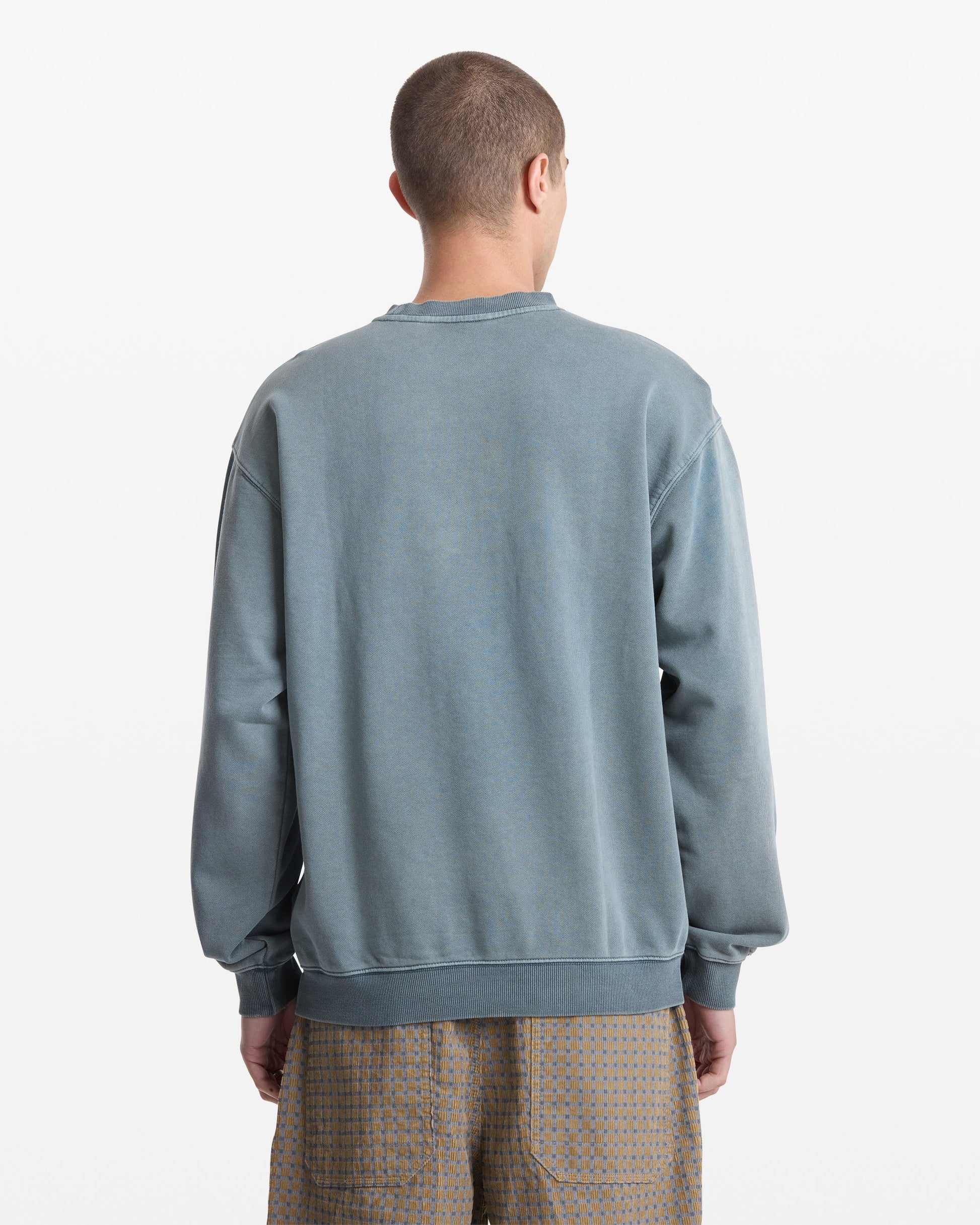 A person with short hair, seen from behind, wears the Volcom Men's Smoothie Crew sweatshirt in faded blue-gray and light brown patterned shorts against a plain white background.