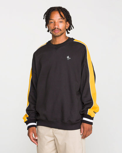 A man with short, twisted hair and a neutral expression stands against a plain background, wearing the Volcom Men's Flying Hi Crew—a black sweatshirt featuring brushed-back fleece and colorblocked sleeves with yellow and white stripes—paired with beige pants. This sweatshirt is crafted from REPREVE recycled polyester for an environmentally conscious touch.