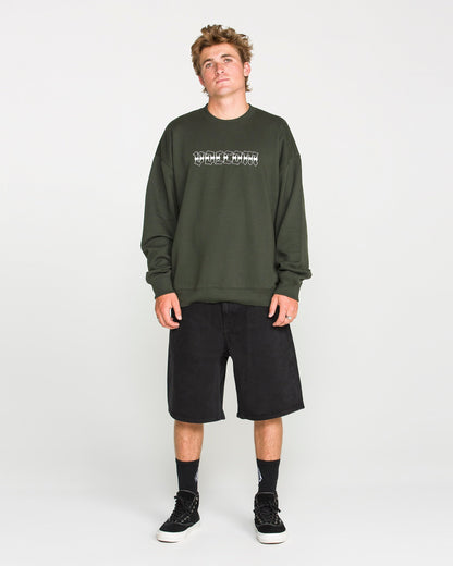 A young man wears the Volcom Men's Dirty Work Crew, a dark green crew sweatshirt crafted from recycled polyester with a graphic design, paired with black knee-length shorts, black socks, and black sneakers as he stands against a plain white background. The loose fit fleece provides both comfort and style for a laid-back, casual look.
