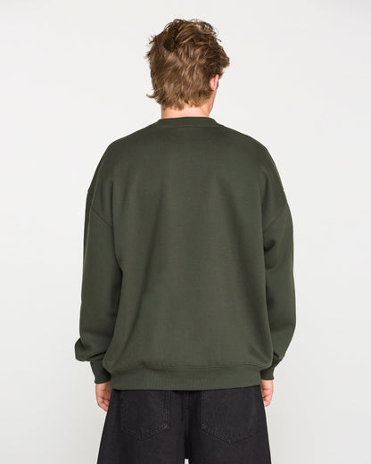 A person with short, light brown hair is facing away from the camera, wearing the Volcom Men's Dirty Work Crew—an oversized green sweatshirt crafted from recycled polyester—paired with black pants against a plain white background.