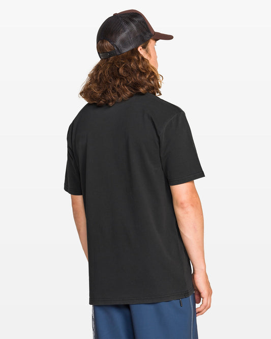 A person with long, curly brown hair is seen from behind, wearing a Volcom Men's Proto Type Short Sleeve Tee in black, navy blue shorts, and a black mesh cap against a plain white background.