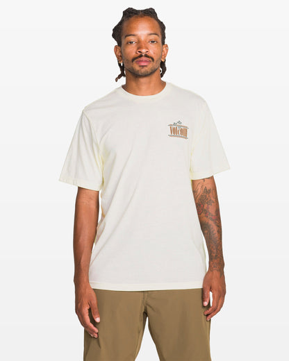 A person with dreadlocks and tattoos on their right arm wears the Volcom Men's Breathe Deep Short Sleeve Tee in heather, featuring a small left chest graphic, paired with khaki shorts, standing against a plain white background.