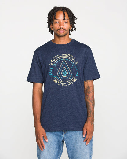 A person wearing a Volcom Men's Line Feld Short Sleeve Tee in navy blue heather, made from soft ring spun cotton, and light blue jeans stands against a plain white background, looking at the camera with a neutral expression.