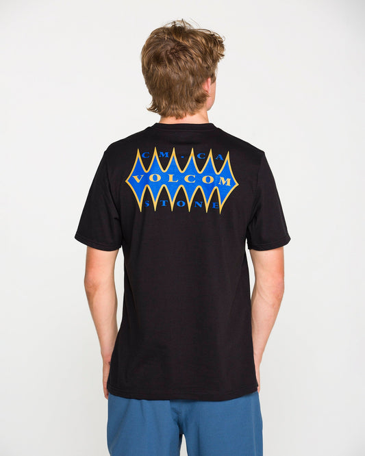 A person with short brown hair, wearing the Volcom Men's Smokers Lounge Short Sleeve Tee in washed black heather—with a blue and yellow Volcom Stone graphic on the back—stands facing away from the camera.