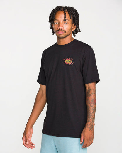 A man with short dreadlocks is wearing the Volcom Men's Spf91 Short Sleeve Tee in a black, medium-weight heather. The shirt features a small sun and eye graphic on the chest and is designed with a modern fit, crafted from a soft ring spun cotton-poly blend for everyday comfort. He stands against a plain white background.