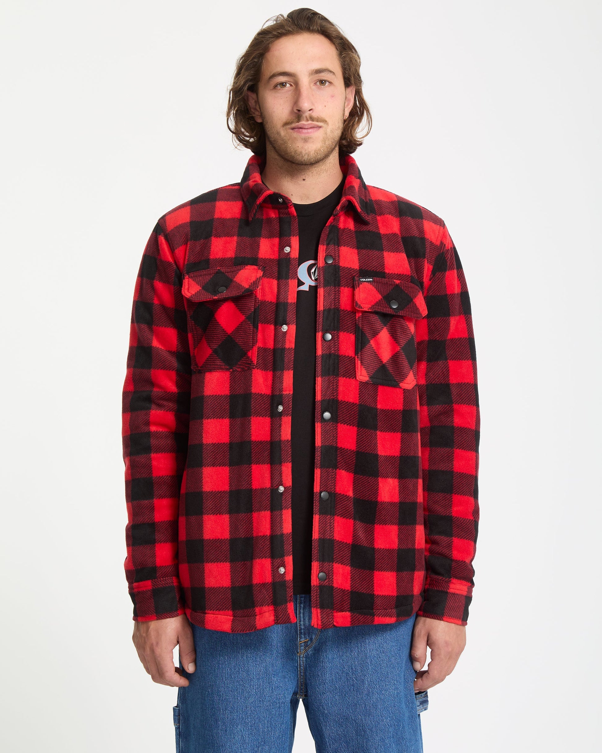 A man stands facing forward against a white background, wearing the Volcom Men's Bowered Fleece Long Sleeve in red and black plaid over a black t-shirt and blue jeans.