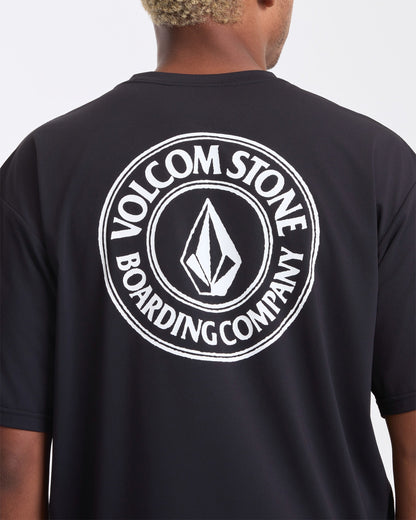 A man wearing the Volcom Men's Drain You Short Sleeve Tee, featuring a large white circular Volcom Stone Boarding Company logo and diamond emblem on the back—perfect for aquatic adventures.