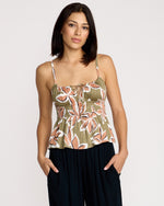 A woman with straight dark hair wears the Volcom Women's Psychonic Cami with adjustable straps and black pants, standing with her hands in her pockets against a plain light background.