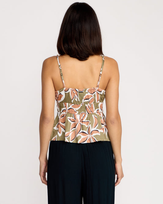 A woman with shoulder-length dark hair is seen from the back, wearing the Volcom Women's Psychonic Cami with a floral print and adjustable straps, paired with black pants against a plain white background.