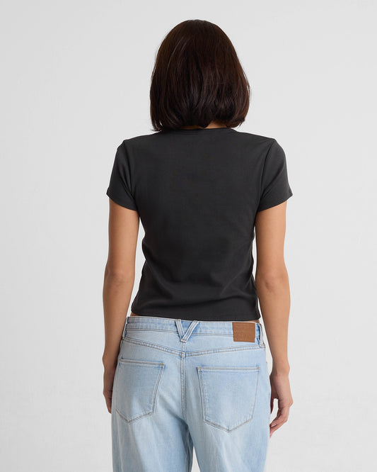 A woman with shoulder-length dark hair, seen from behind, wears the Volcom Women's Have A Clue Tee in black and light blue jeans against a plain white background.